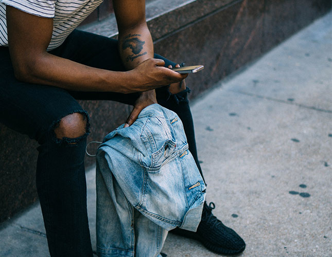 FAQs Man holding jacket sitting on step on mobile phone outside