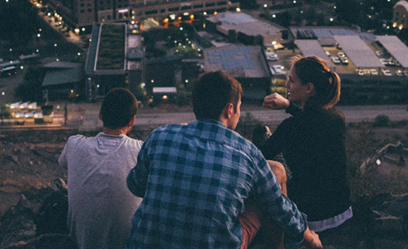 careers-join-team square.jpg 3 young adults sat on a hill at night looking over a town